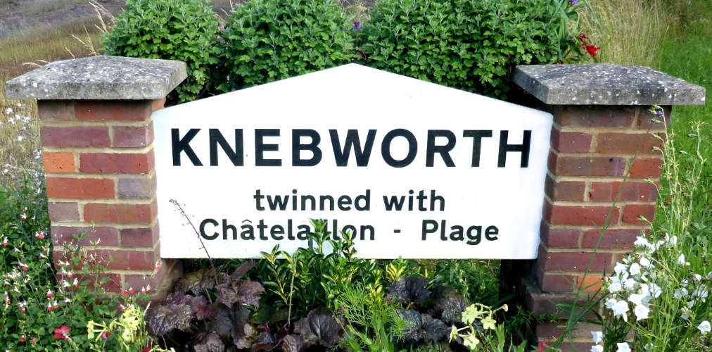 This image: A photo of the sign at the entrance to Knebworth,
					surrounded by flowers. The sign reads: Knebworth twinned with
					Chatelaillon-Plage. The map: a bird's eye view of Knebworth south of
					Stevenage, with a flashing gold map marker over the site, with the
					label: Swangleys Green, Land off Watton Road.